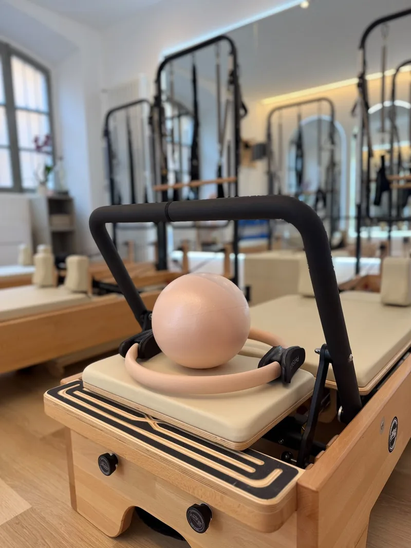 Dettaglio di un reformer con una palla e un anello da Pilates color pesca, e lo studio luminoso sullo sfondo